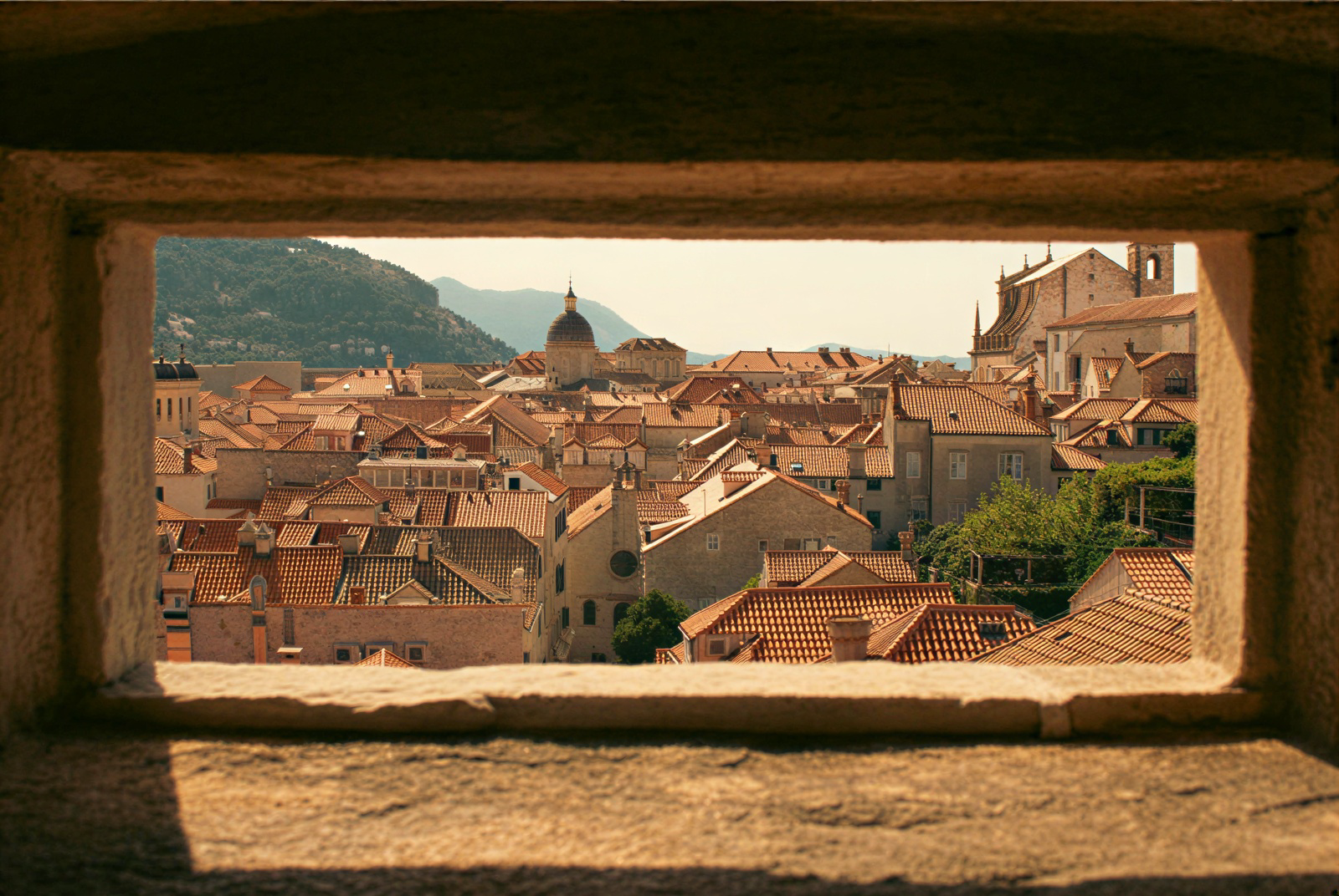 Rooftops of a Mediterranean town seen through an opening in a stone wall